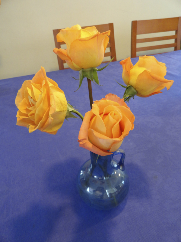 Rosas anaranjadas, en jarrita de vidrio soplado, en color azul tornasolado, adquirida en un bazar y mantel de damasco comprado en Zara Home. Fotógrafa Lilia Martínez.